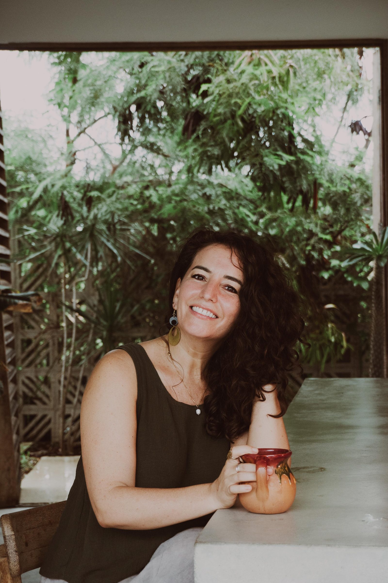 Michelle, smiling, seated at a table in front of greenery