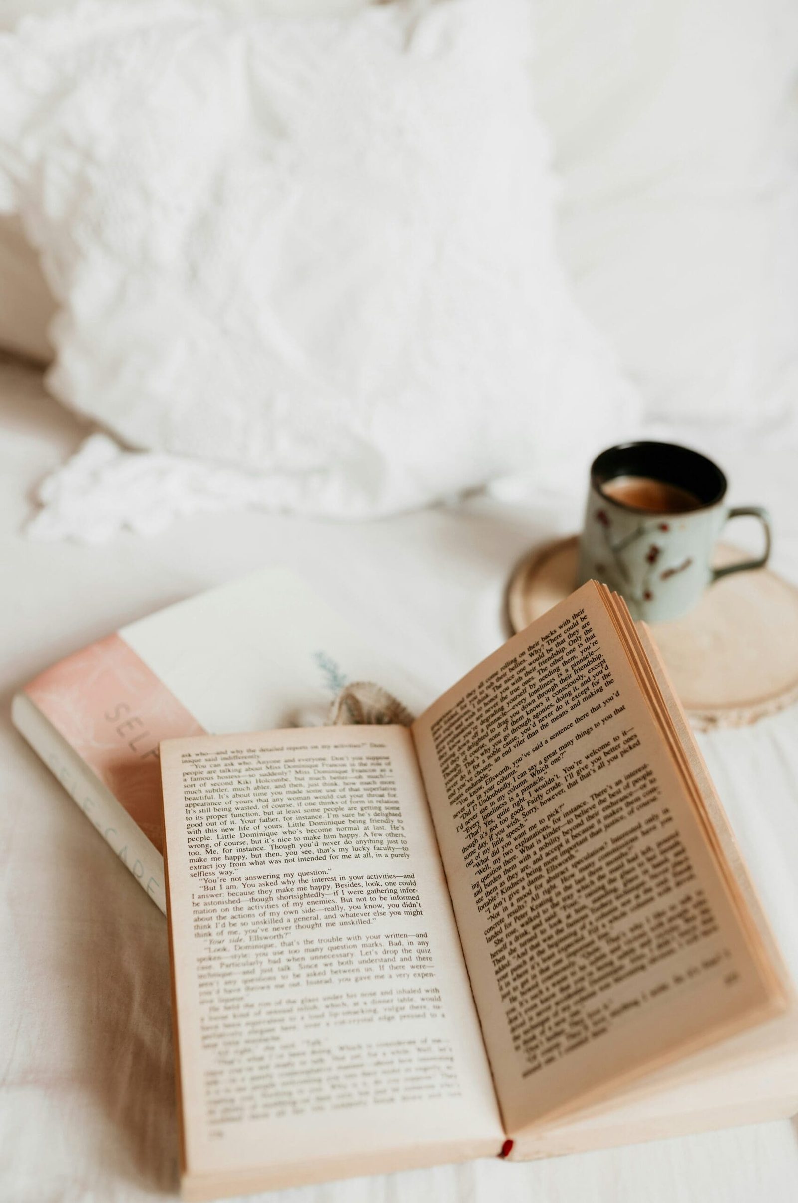 Open book and cup of coffee on a cozy bed with soft pillows, creating a calm reading atmosphere.