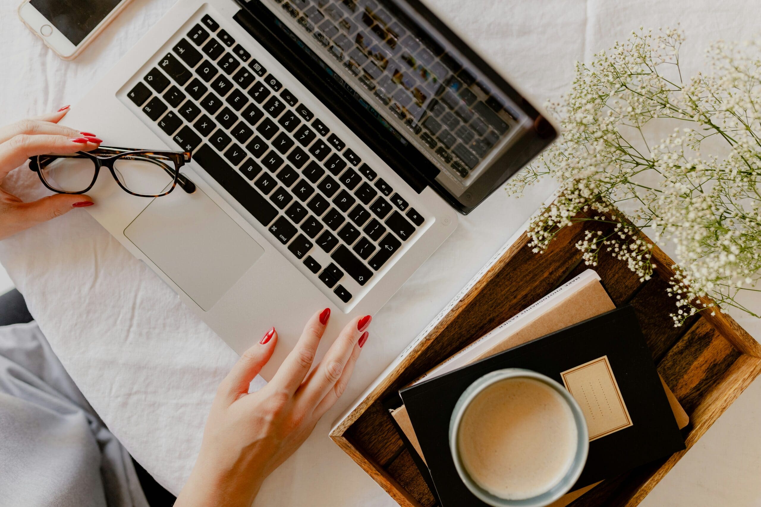 Woman working on laptop with coffee and notebooks, representing balance, creativity, and the freedom of building a virtual wellness business.