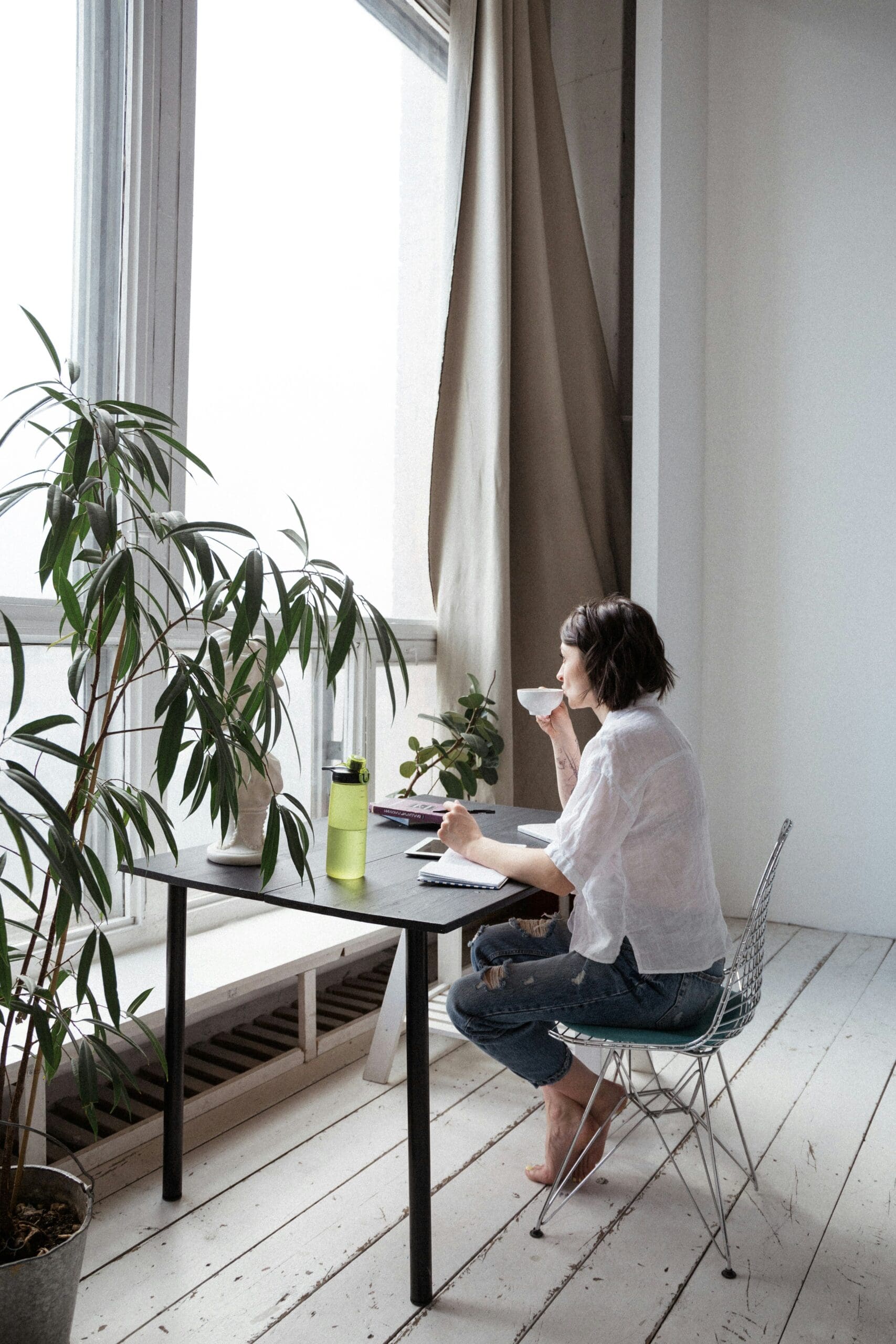 Freelancer enjoying morning coffee while planning the day at a bright home office desk with plants.