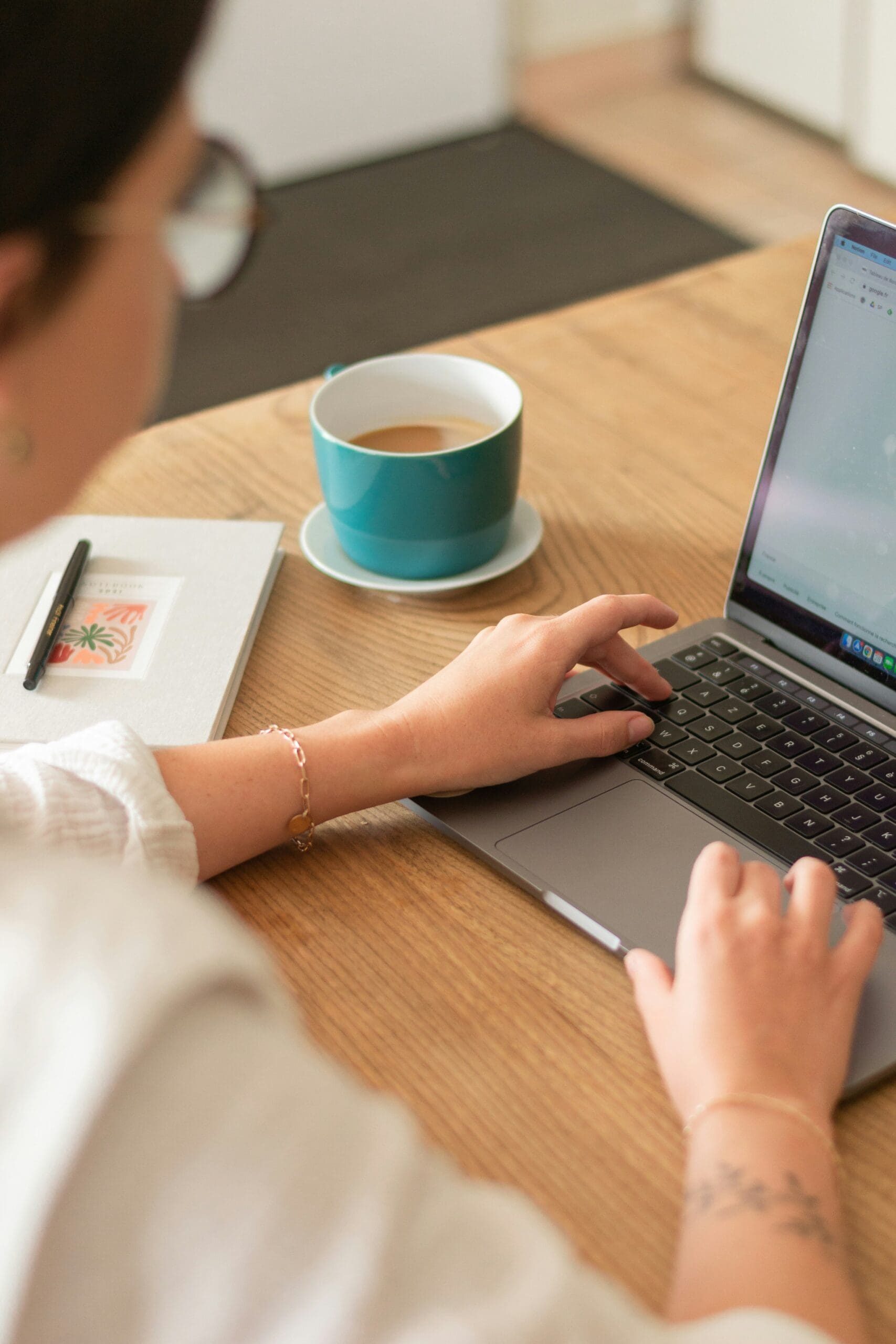 Woman working from home on laptop with coffee cup and notebook on desk – calm and productive workspace setup.