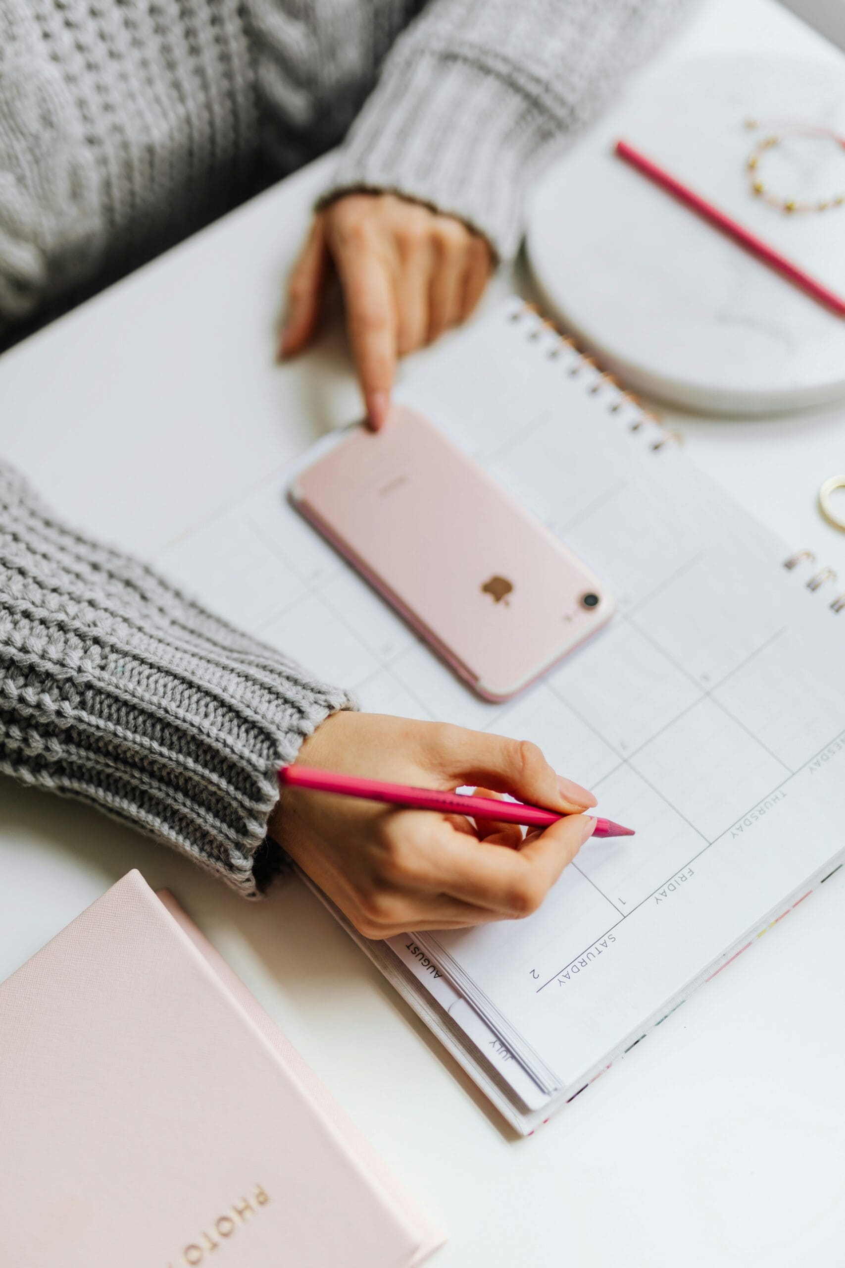 Woman planning her week in a pink planner with a pencil and smartphone on the desk.